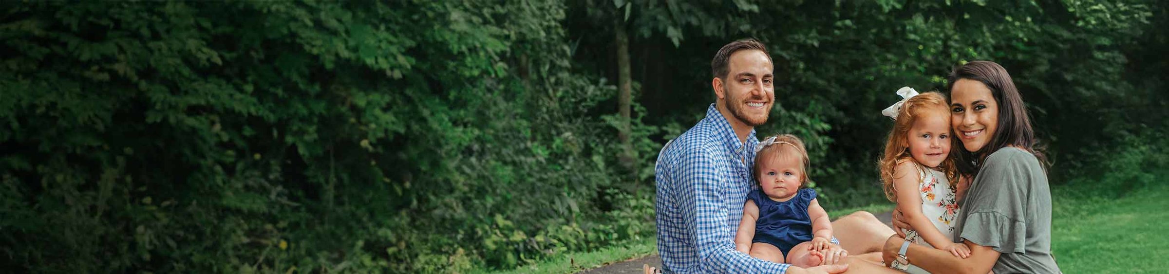 Ellie, a child with SMA, sitting outside on her father's lap next to her mother and sister