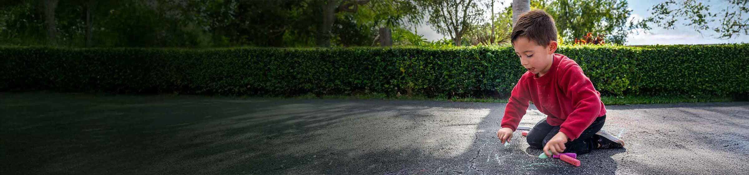 A picture of Matteo, a child with SMA, drawing with chalk on a driveway