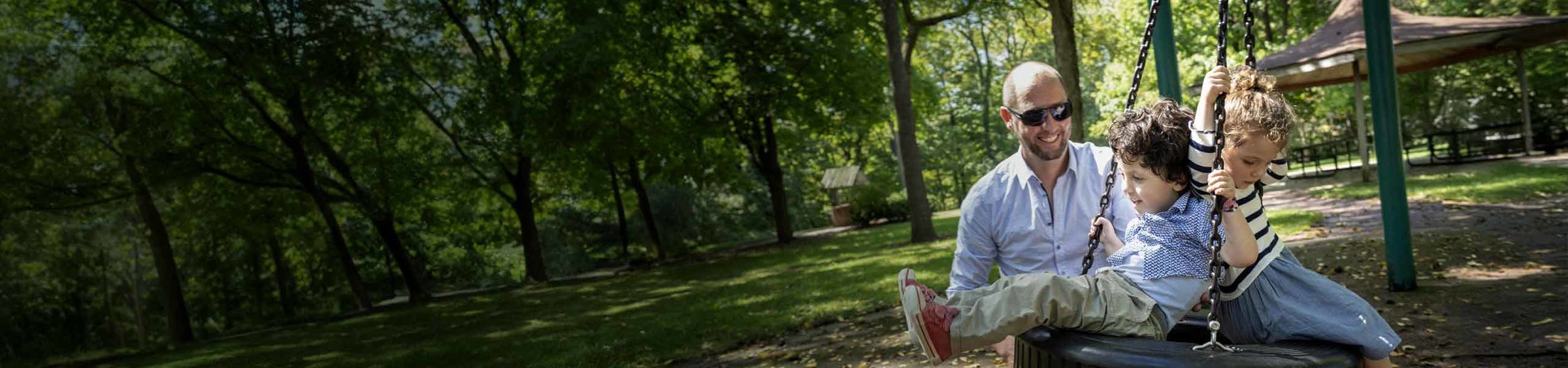 Louis, a child with SMA, sitting on a tire swing with his sister as their father, Marco, pushes the swing