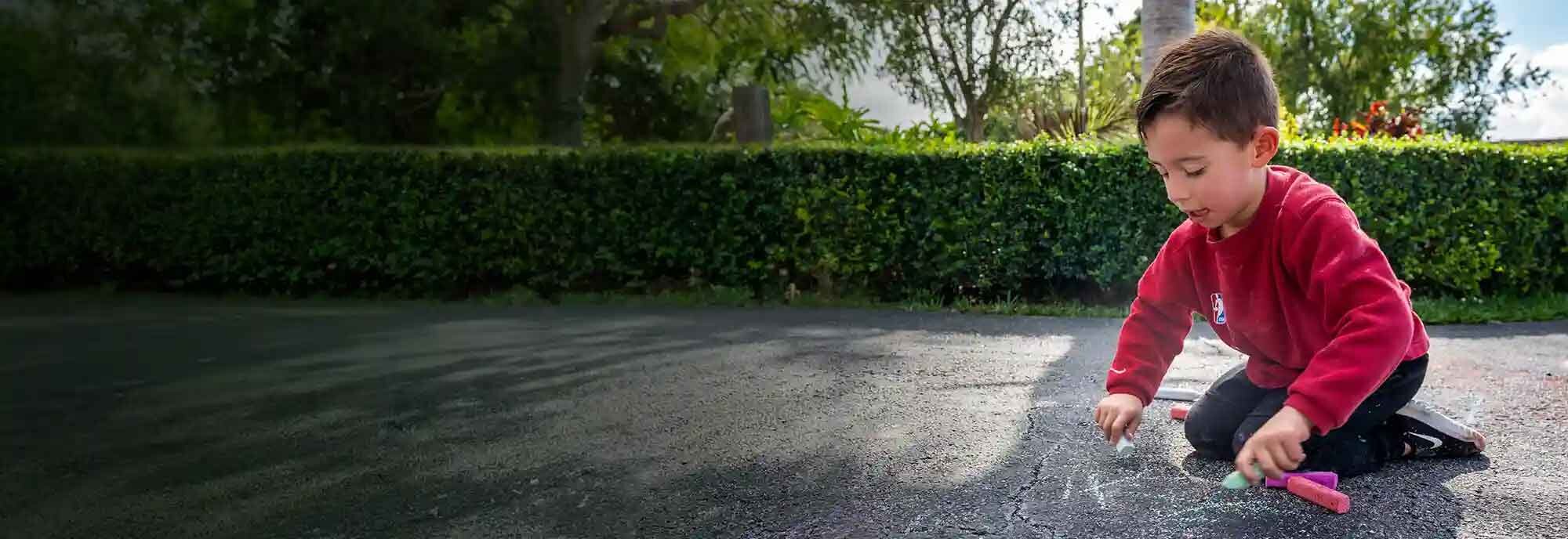 A picture of Matteo, a child with SMA, drawing with chalk on a driveway